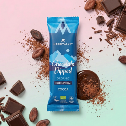 Moonvalley Organic Protein Bar Chocolate-Dipped Cocoa surrounded by chocolate pieces and cocoa beans